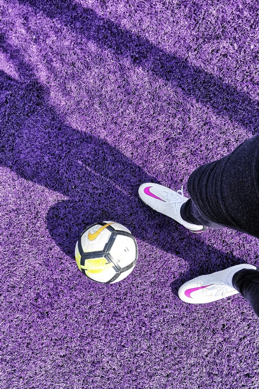 person wearing white slippers standing next to a soccer ball on purple carpet