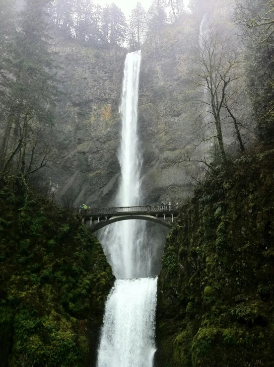 a man riding a surfboard under a waterfall next to a bridge