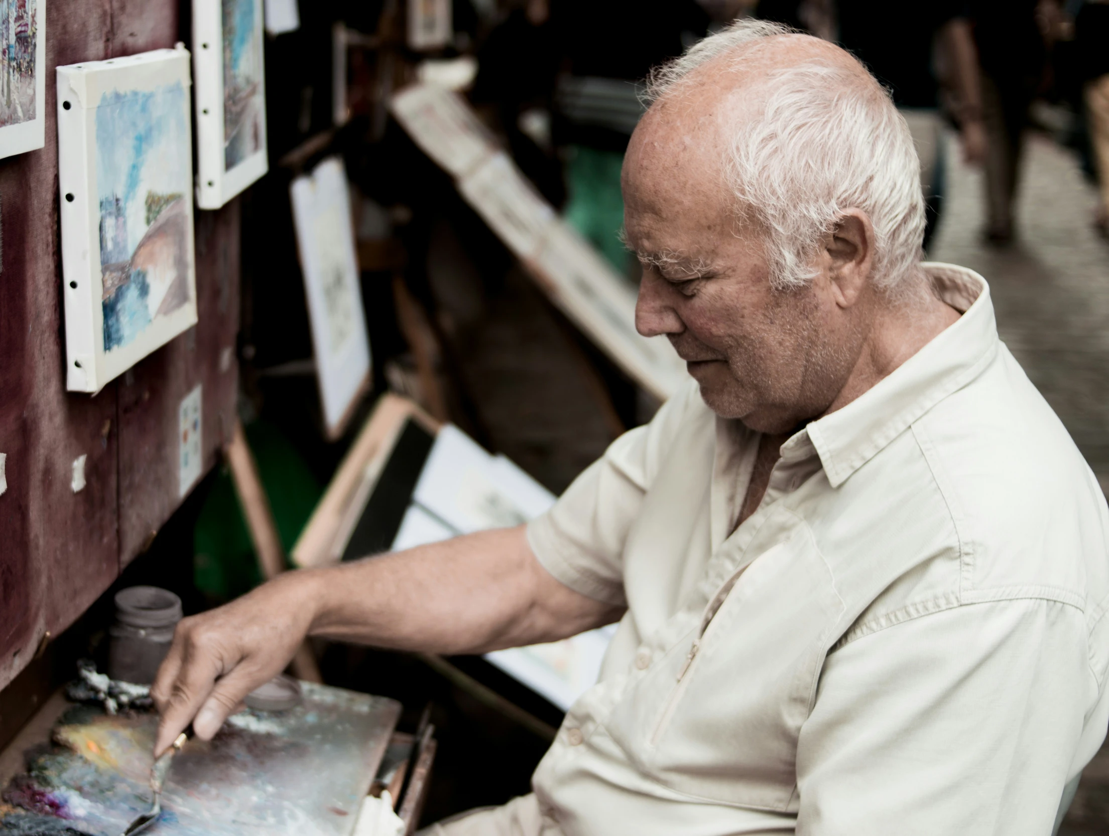 an older man sits at a desk near multiple painting supplies