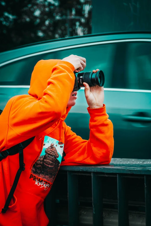 a man wearing an orange hoodie sitting down with his camera