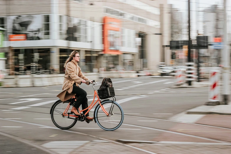 a woman with brown coat riding a bike down the street