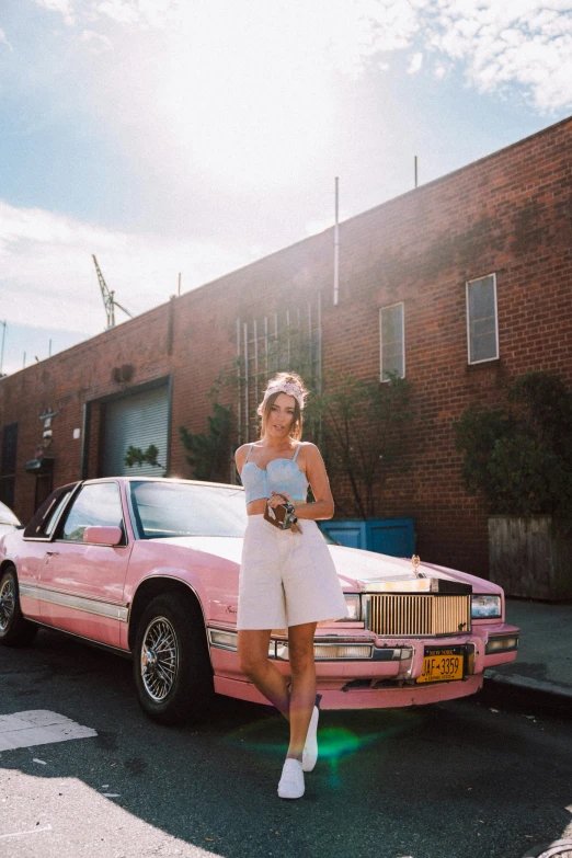 a girl stands next to a pink car in the street