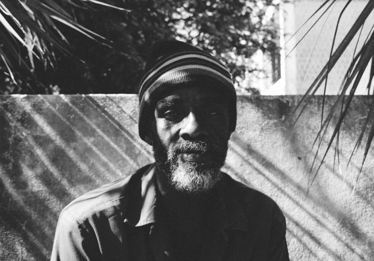 man with beard and hat leaning against wall