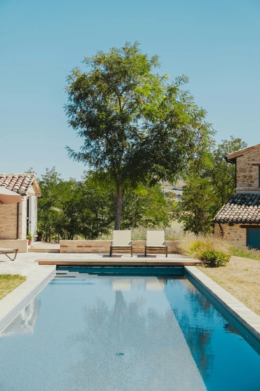 a small, long rectangular pool surrounded by lawn chairs and bushes