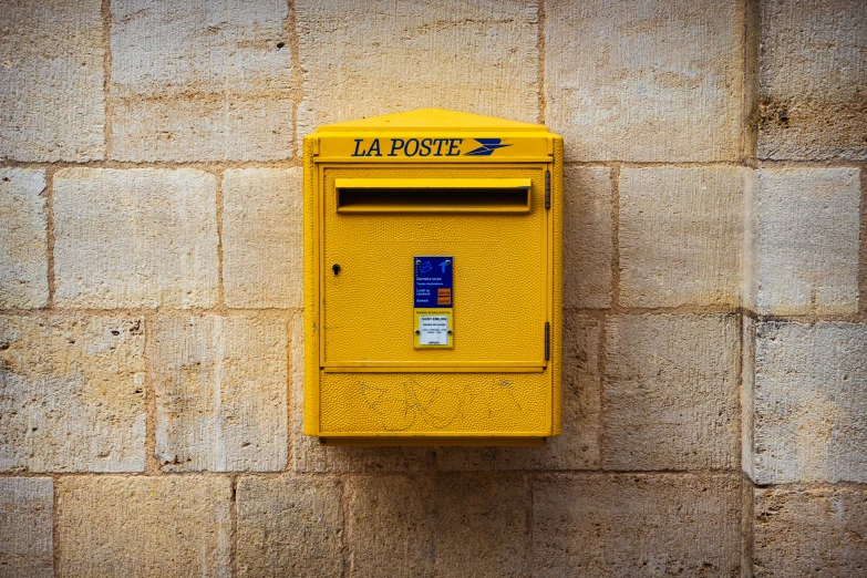 a bright yellow mailbox is mounted on the side of a stone wall