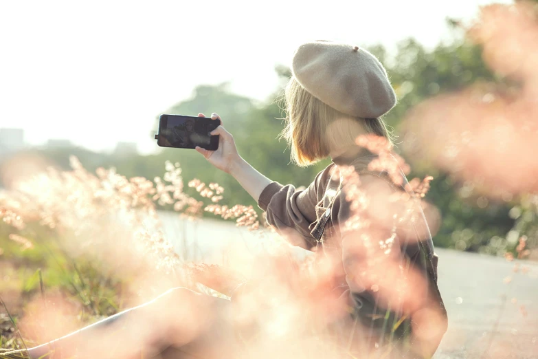 a woman sitting in the grass holding up her camera