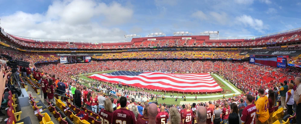 a large american flag being held up in a football stadium