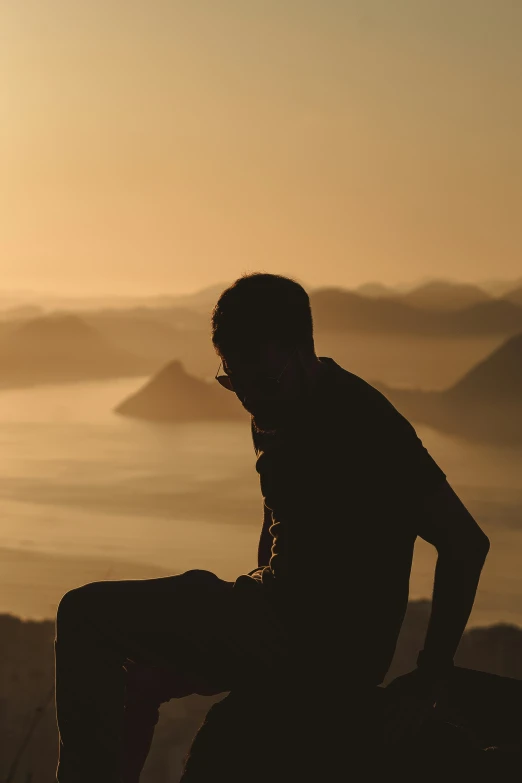 a man sitting on a mountain while looking at the sunset