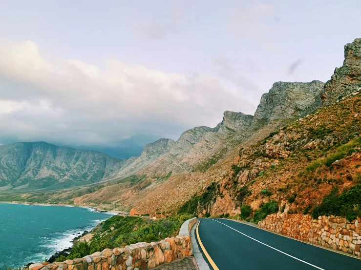 a view of the water from the side of the road, with a large cliff in the distance