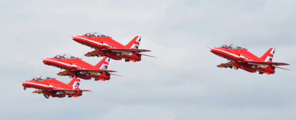 four red planes fly overhead on cloudy day