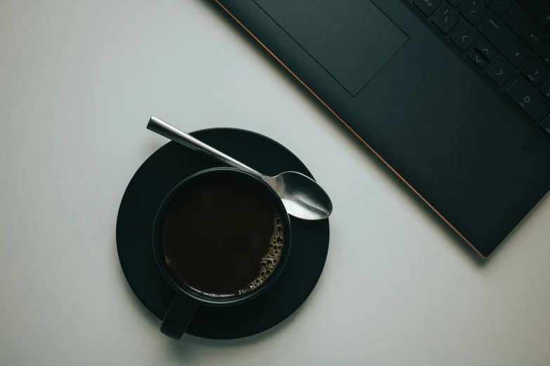 the coffee cup and saucer is beside a laptop