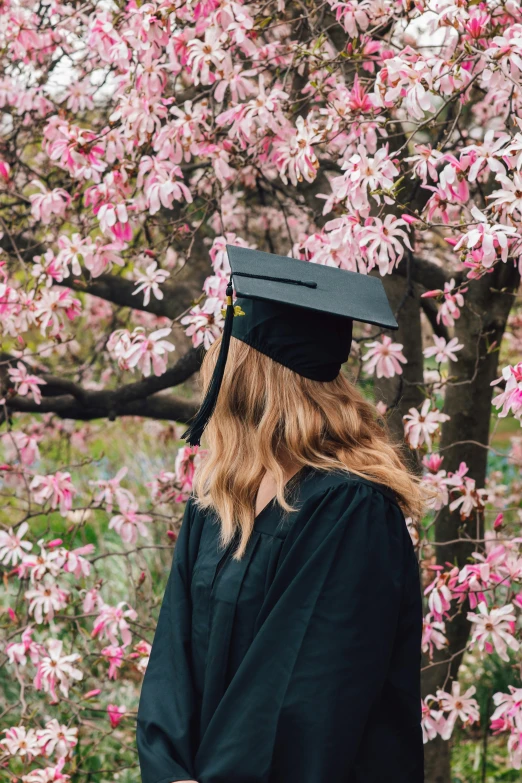 a person in cap and gown standing by flowering tree