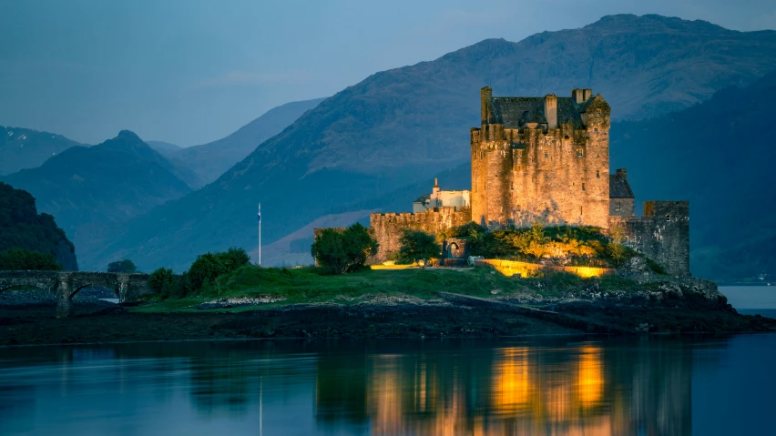 a castle is lit up at night, near a mountain