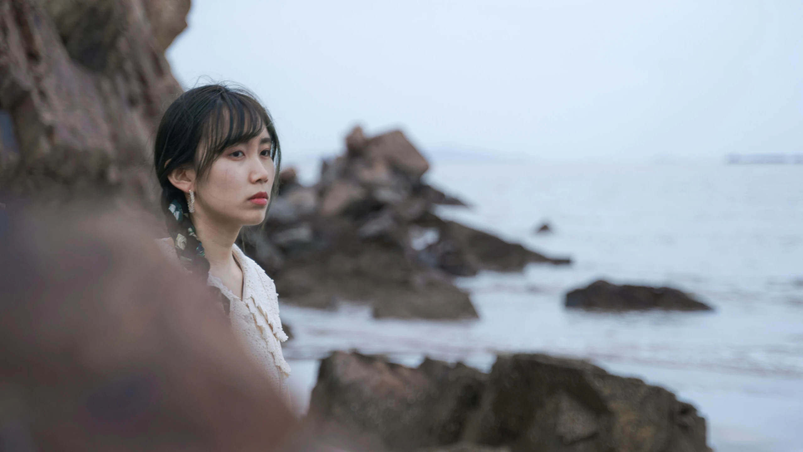 an asian woman standing next to the ocean near rocks