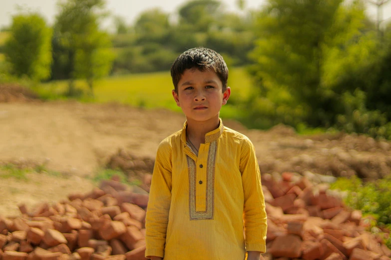 a little boy wearing a yellow shirt and standing near a pile of bricks