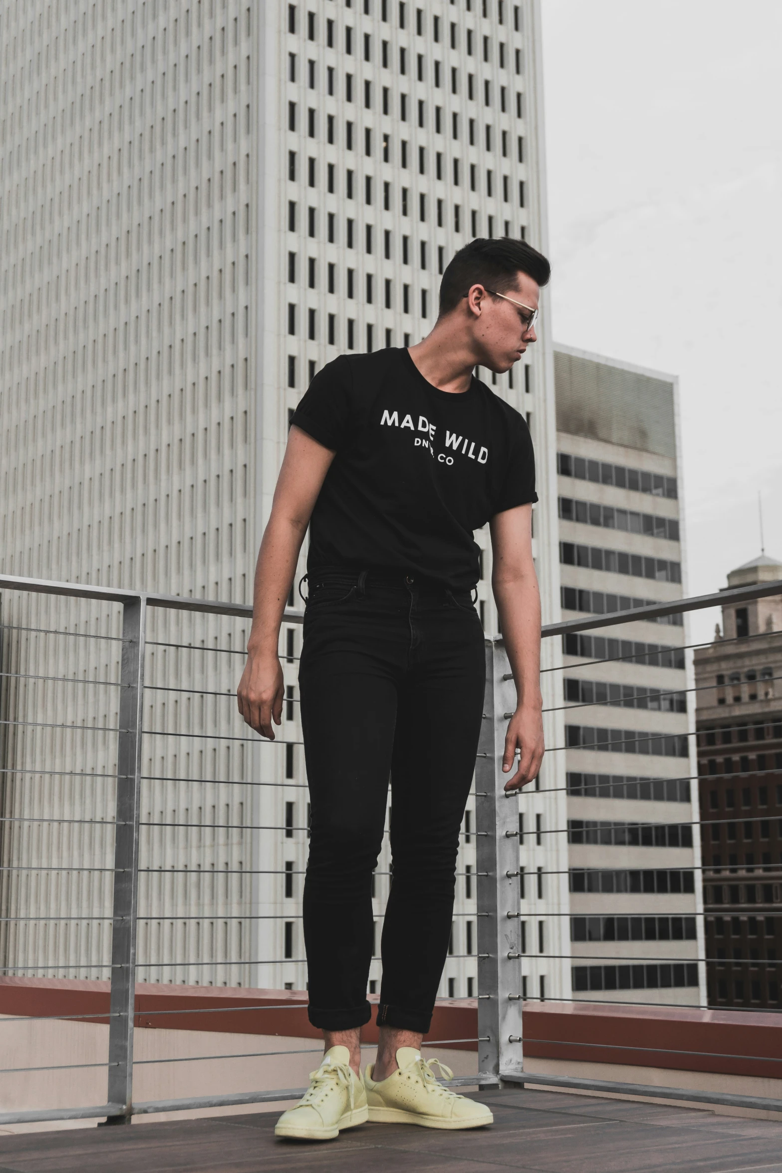 a young man standing next to a fence wearing tennis shoes