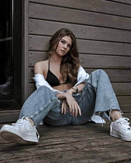 a woman sitting on the ground in jeans with her legs crossed