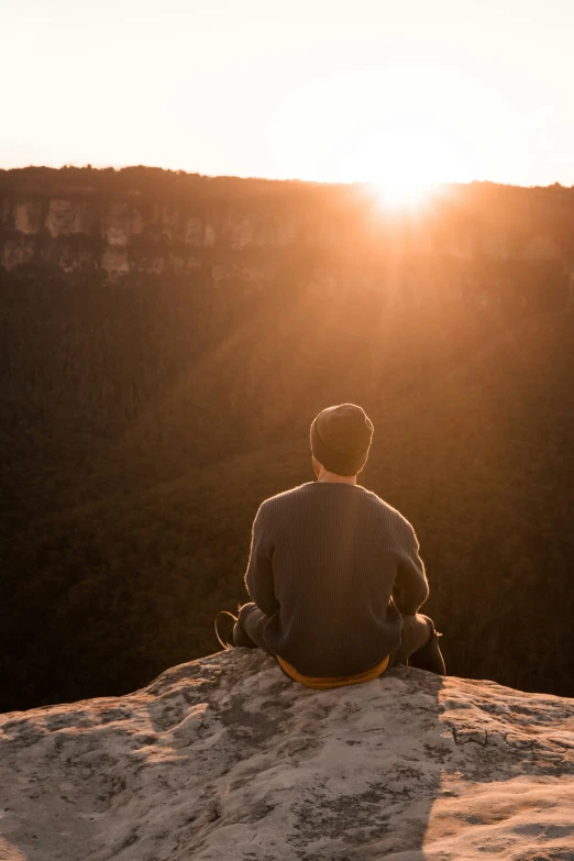 a man sitting in the sun on top of a mountain