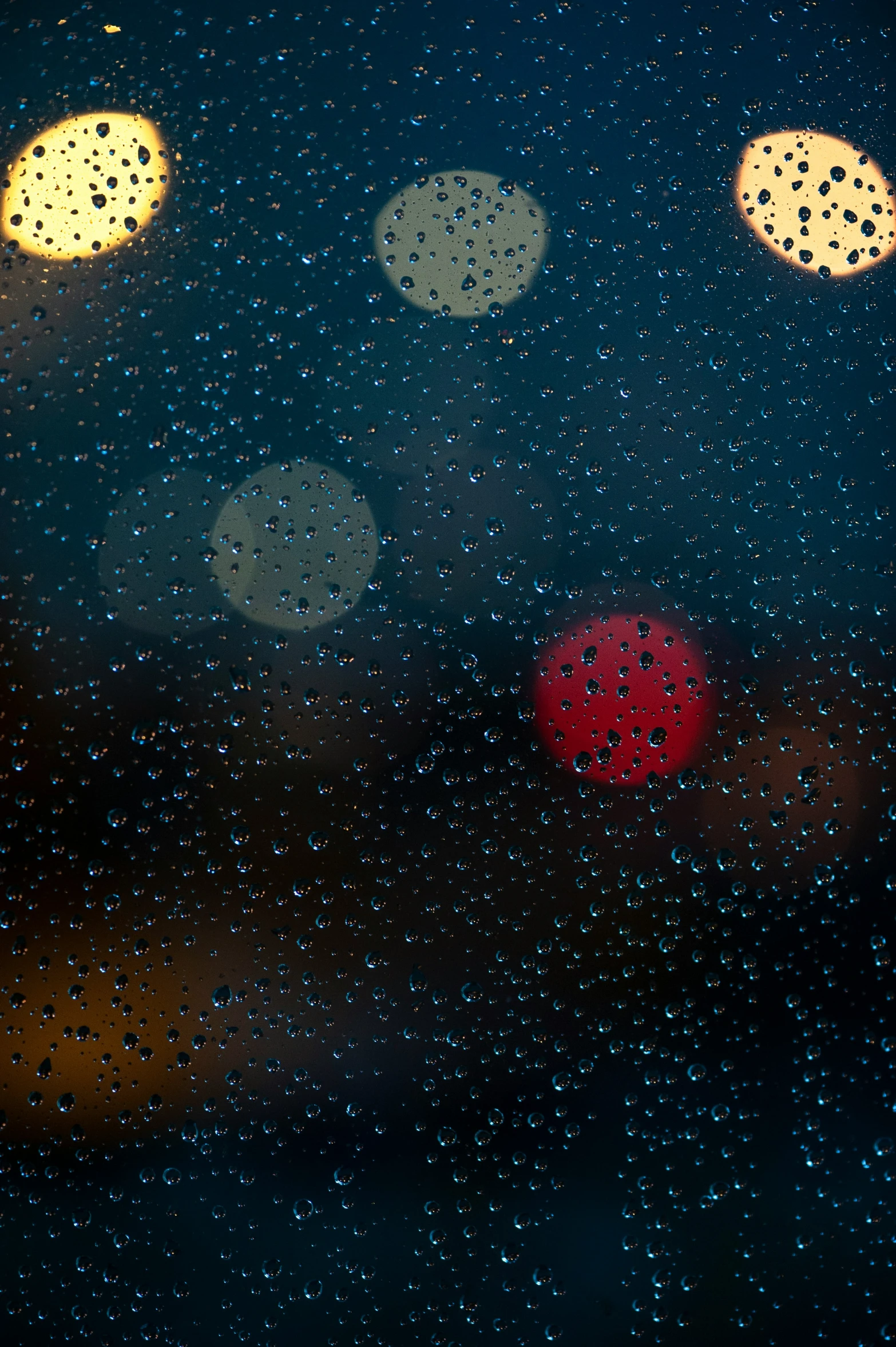 traffic lights are shown through the rain on a window