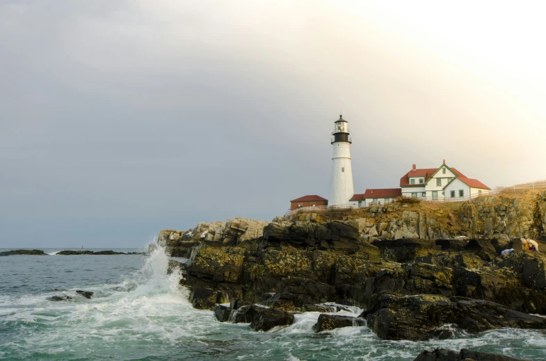 a white light house with red roof on the top of a rock