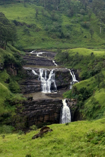 water fall with green hills and trees in background