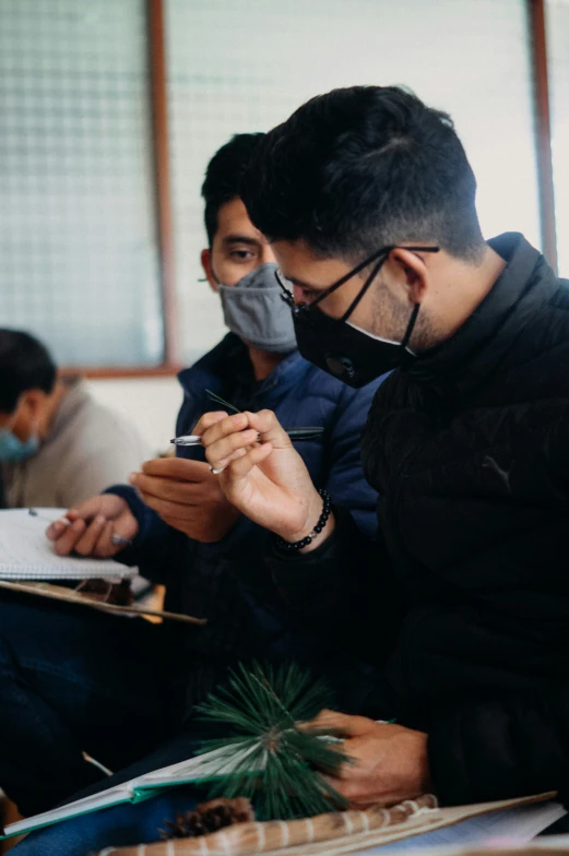 two men with face masks sit down and look at their phones