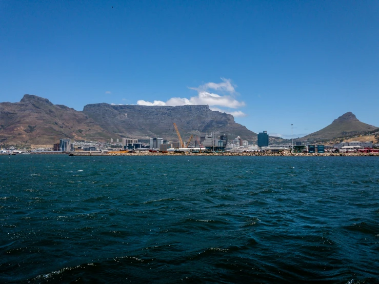 the water is glistening in the morning with mountains and buildings in the background