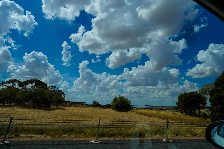 a view out the window of a vehicle driving on a rural road, with clouds in the distance