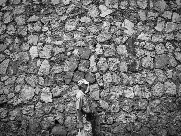 a man standing in front of a stone wall with another person holding a bag