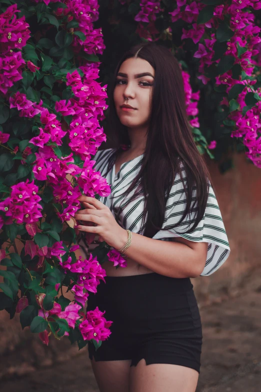 a girl in high waisted shorts stands by a bush with purple flowers