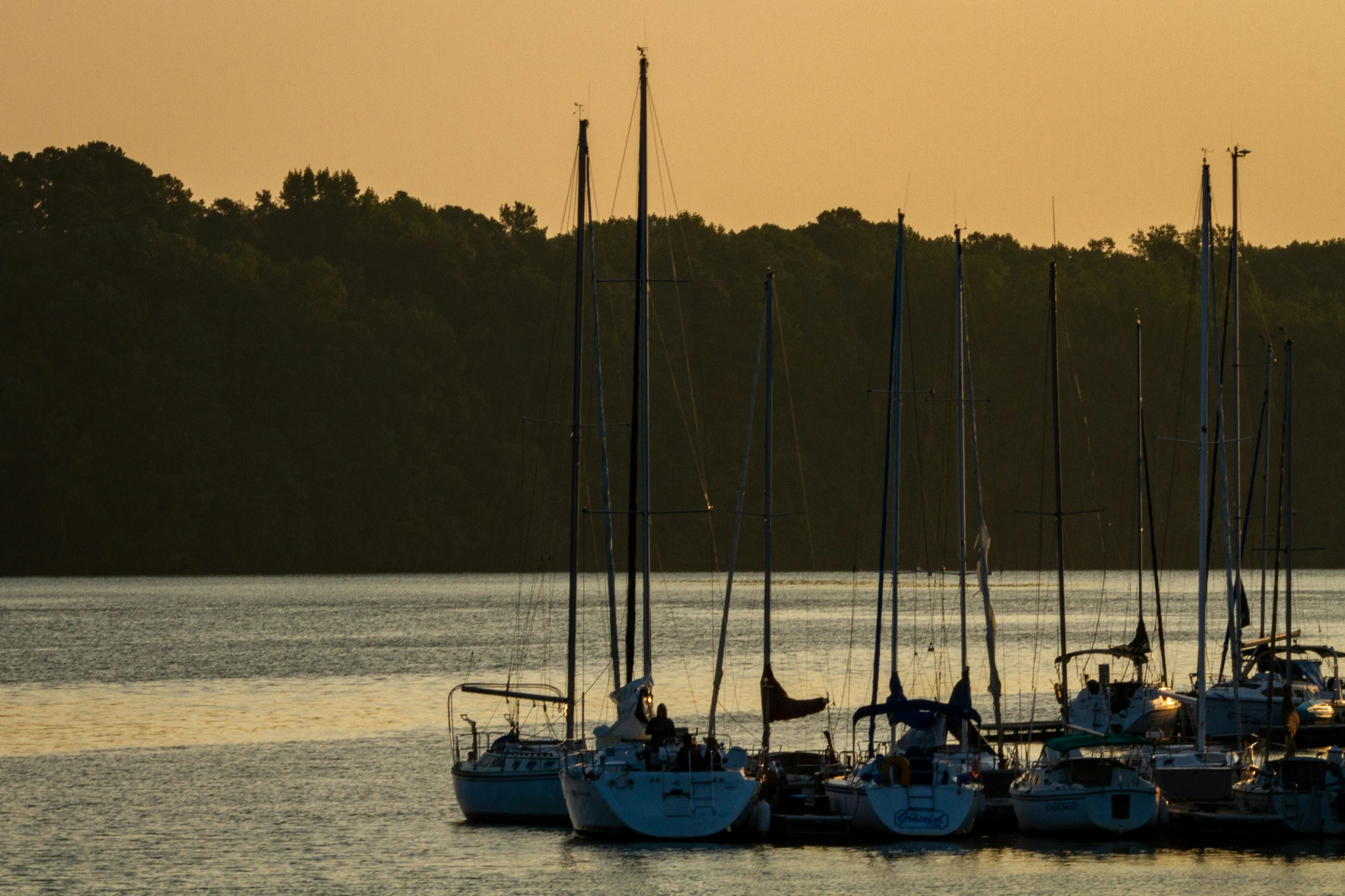 a fleet of boats floating in the middle of a lake at sunset