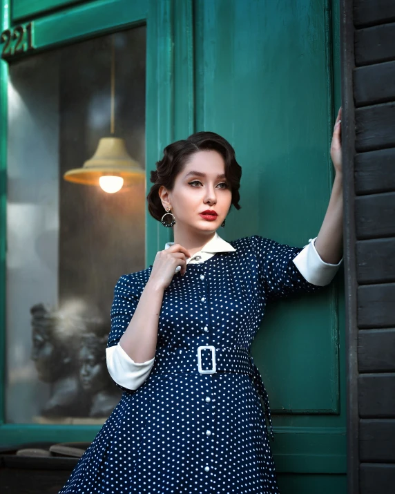 a woman posing against a green door with her hands on the side of the door