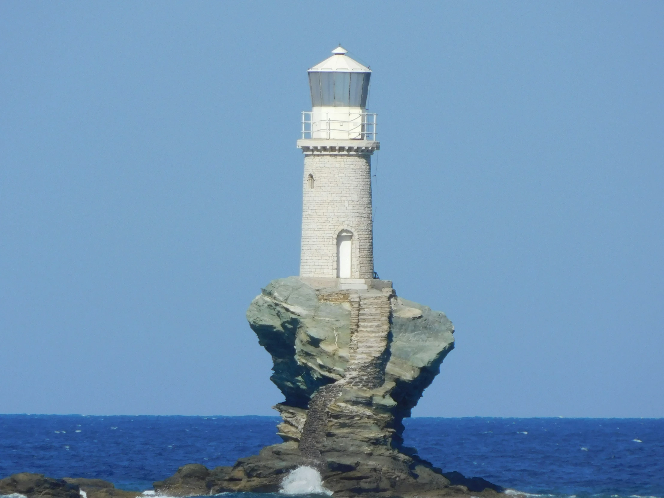 a large rock by the ocean with a lighthouse on top