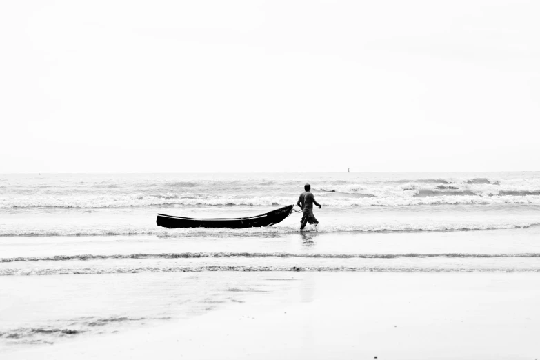a man walking out to the ocean while holding a boat