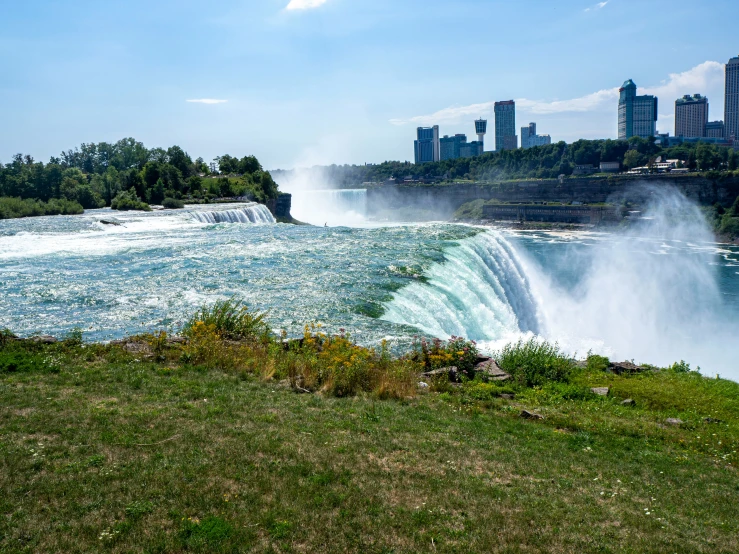 a water fall on the side of a lake with buildings in the background