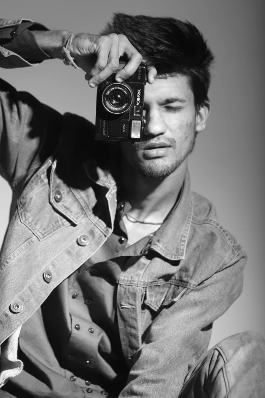 black and white pograph of man with jean jacket holding a camera