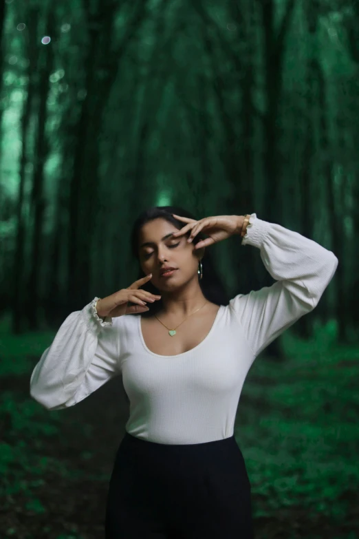 a woman standing in a wooded area wearing a white top