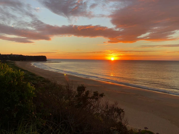 a beach is shown at sunset, with the sun just starting to set