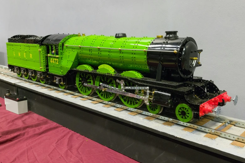 a green and black train on tracks next to display case