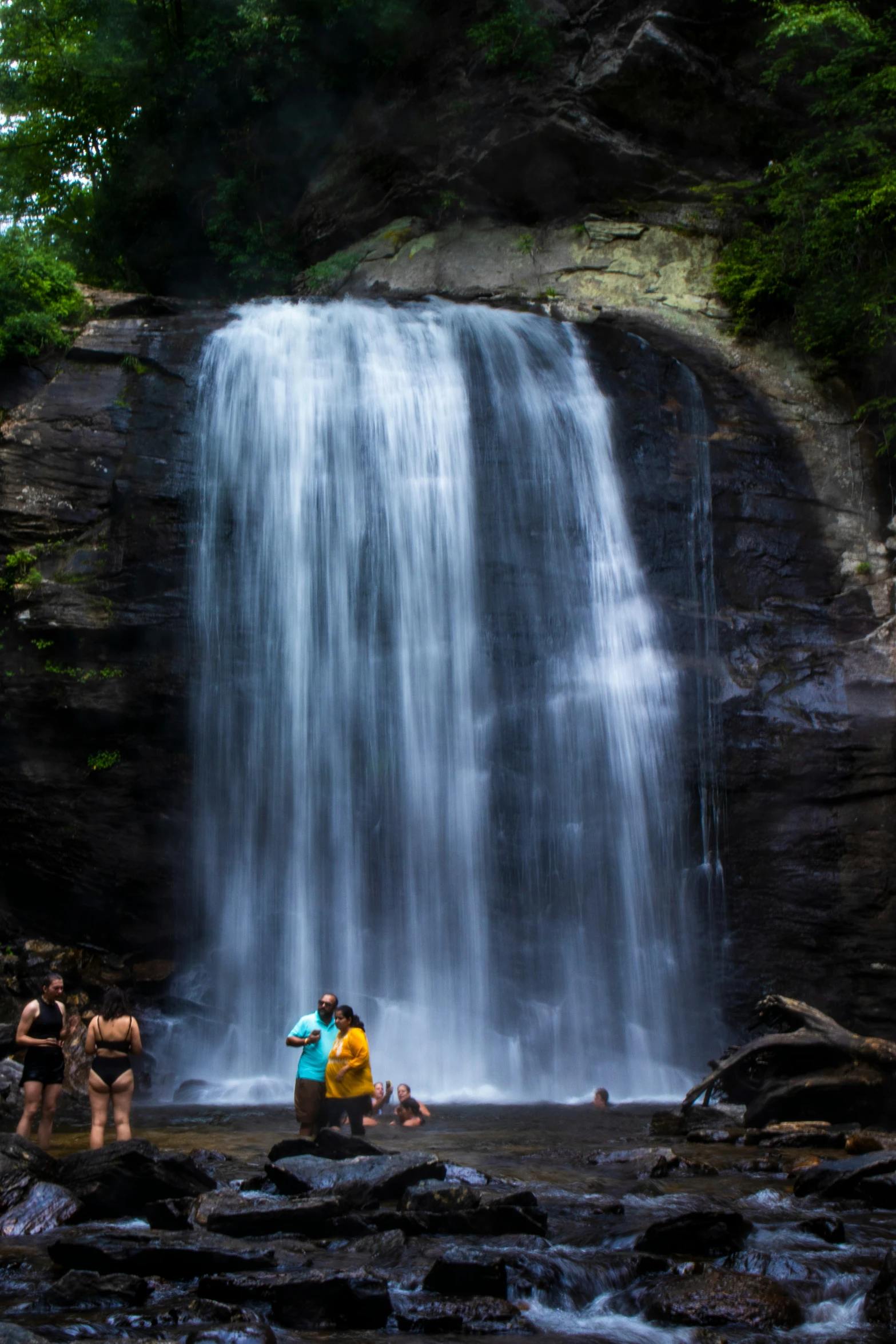 two women and one man standing under the waterfall