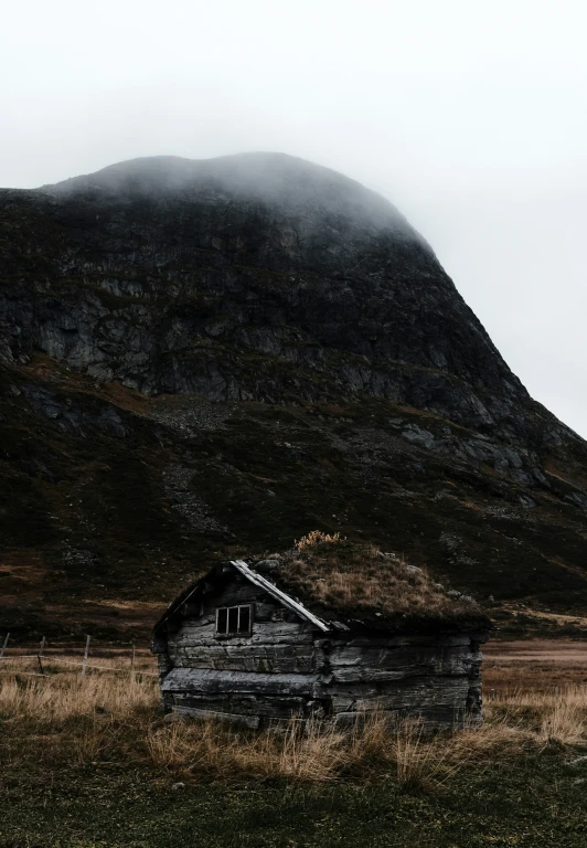 a wooden building in a field with hills in the background