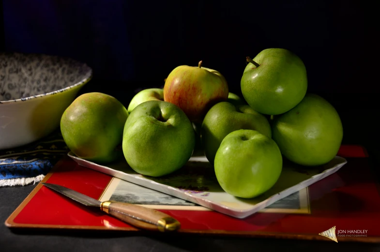 a bowl of green apples sits on a serving tray