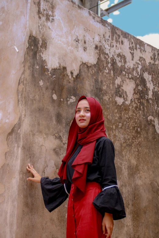 woman wearing hijab standing by old stone wall