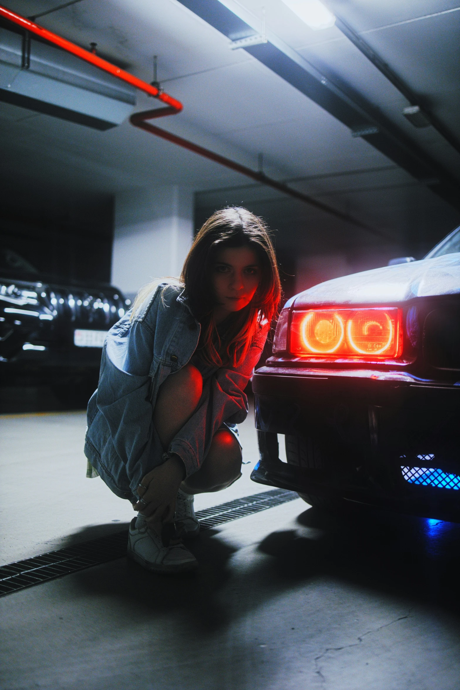 a girl leaning against a car in an underground garage