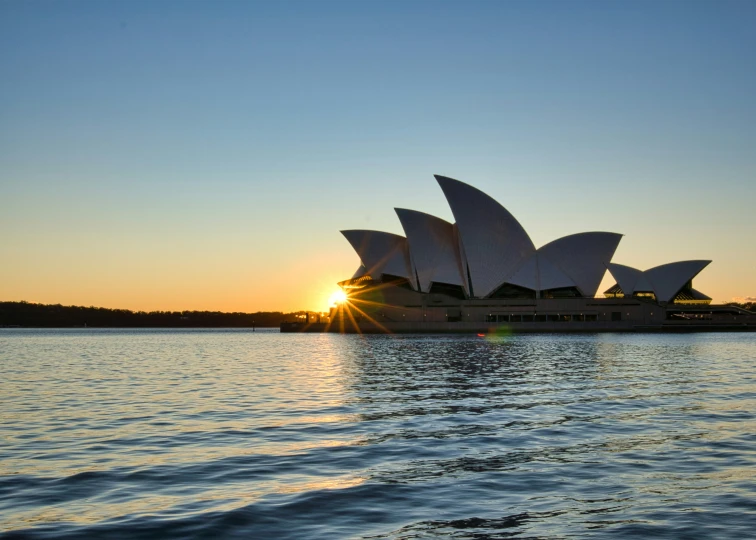 the sun sets behind a large opera house in sydney