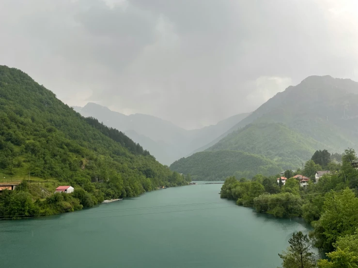 mountains are in the background, a river is on one side and a row of houses is on the other