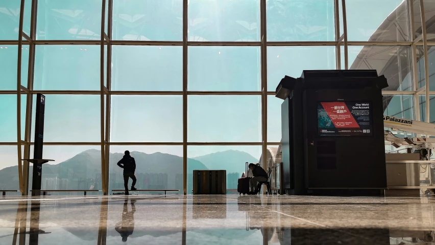 a man standing in front of large windows next to a luggage claim