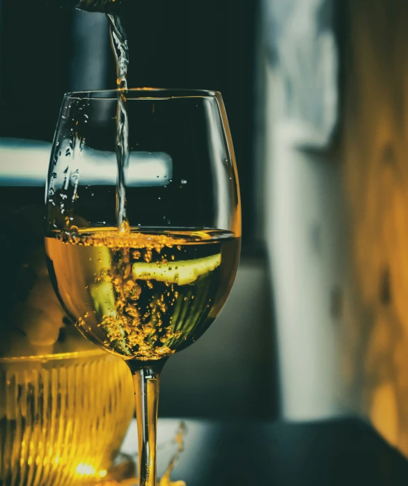 a glass filled with white wine being poured