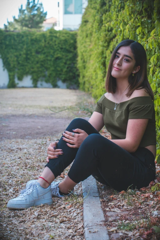 a young woman is sitting outside by some bushes