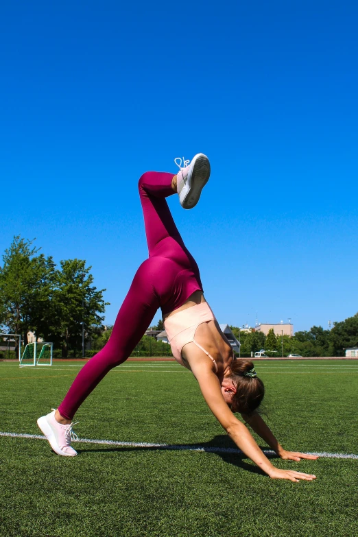 woman in pink doing handstand on a grass field